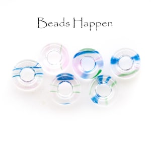 May include: Six clear glass beads with colorful swirls of blue, green, and pink. The beads are round with a hole in the center. The text "Beads Happen" is written above the beads.