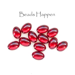 May include: A group of red glass beads, scattered on a white surface. The text "Beads Happen" is written above the beads.