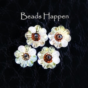 Puede incluir: Cuatro cuentas iridiscentes de color blanco en forma de flor con un centro de cobre. Las cuentas están sobre un fondo negro. "Beads Happen" está escrito en blanco sobre las cuentas.