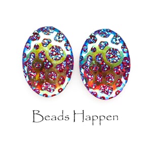 Puede incluir: Un par de pendientes ovalados con un acabado brillante e iridiscente. Los pendientes tienen un esquema de color azul, verde y rosa sobre un fondo blanco. Los pendientes están hechos de vidrio y tienen una superficie texturizada. "Beads Happen" está escrito en negro debajo de los pendientes.