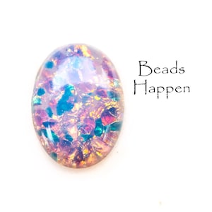 Op de afbeelding: Een close-up van een roze, iriserende, ovale glazen kraal met gouden en groene vlekken. De kraal ligt op een witte achtergrond. De tekst "Beads Happen" is zichtbaar in de rechterbovenhoek van de afbeelding.