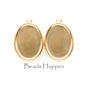 May include: Two gold-colored oval pendant trays with a loop at the top for attaching to a chain or other jewelry component. The trays have a flat surface for adding a design. The text "Beads Happen" is at the bottom.
