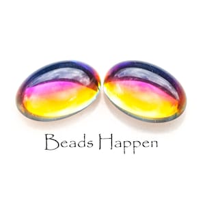 Puede incluir: Dos cuentas de vidrio ovaladas iridiscentes con un degradado de colores amarillo, rosa y azul. Las cuentas están sobre un fondo blanco con el texto "Beads Happen" debajo.
