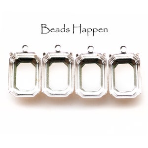Puede incluir: Tres engastes de metal plateados para la elaboración de joyas. Cada engaste tiene una forma rectangular con un borde biselado y un bucle en la parte superior para sujetar una cadena o un cordón.