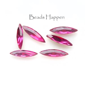 May include: Six pink marquise-shaped glass beads, scattered on a white surface. The beads are faceted and have a glossy finish. The text "Beads Happen" is visible in the top center of the image.