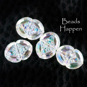 May include: Four iridescent clear glass buttons with a diamond-shaped design. The buttons have a textured surface and are arranged in a semi-circle on a black background. The text "Beads Happen" is visible in the upper right corner of the image.