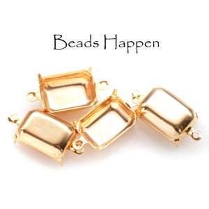 May include: Four gold-coloured rectangular jewellery findings with small loops and decorative feet. The text "Beads Happen" is written in black script above the findings.