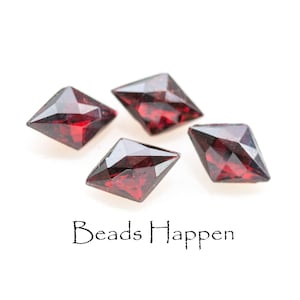 May include: Four faceted, square-cut, deep red gemstones. The gems are arranged on a white background. The text "Beads Happen" is written in a cursive font below the gemstones.