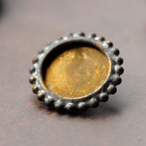 May include: A round, gold-toned metal bezel with a beaded edge. The bezel is designed to hold a small round image or object.