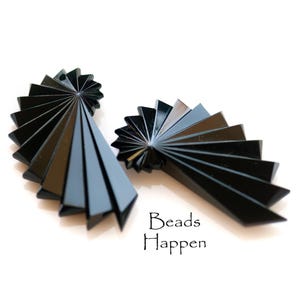 May include: Two black fan-shaped acrylic beads. The beads are made of multiple layers of acrylic that are stacked and angled to create a fan shape. The beads are arranged in a way that they look like they are opening up.