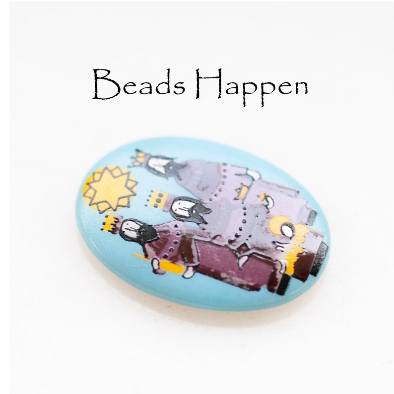 May include: A blue oval-shaped bead with a painted image of the three wise men, a star, and the text "Beads Happen".