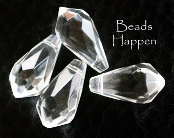 May include: Four clear glass teardrop-shaped beads with faceted edges. The beads are arranged in a pile on a black surface. The text "Beads Happen" is visible in the upper right corner of the image.