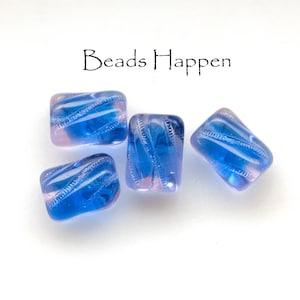 Könnte beinhalten: Vier blaue und rosa Glasperlen mit rechteckiger Form und diagonalem Wirbeldesign. Die Perlen sind transparent, sodass Licht durchscheinen kann. Der Text "Beads Happen" steht über den Perlen.