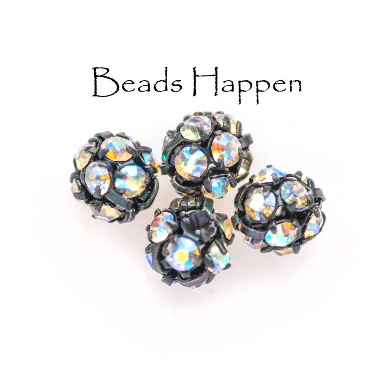 May include: Four black round beads with iridescent rhinestones. The beads are arranged in a cluster on a white background. The text "Beads Happen" is written above the beads.