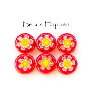 May include: Six red glass beads with a floral design. Each bead features a yellow center, white petals, and a red background. The text "Beads Happen" is above the beads.
