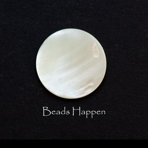 May include: A white, round, smooth, and shiny mother of pearl bead. The bead has a subtle swirl pattern. The text "Beads Happen" is written below the bead.