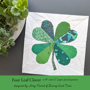 May include: A square, paper-pieced quilt block featuring a four-leaf clover design. The clover's leaves are various shades of green, with patterned fabric accents. The background is white with subtle geometric lines. Text at the bottom reads "Four Leaf Clover a 10" and 12" paper pieced pattern."