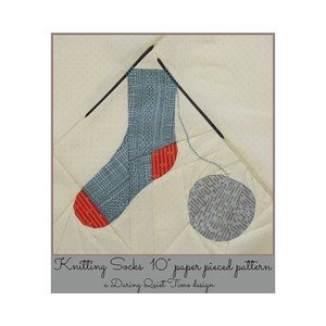 May include: A paper pieced pattern for knitting socks, featuring a blue and red sock with a ball of yarn and knitting needles. The pattern is 10 inches in size and is a During Quiet Time design.
