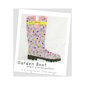 May include: A paper pieced pattern for a garden boot. The boot is grey with a pink and yellow floral print. The boot has a yellow strap with the text "busy Spring".