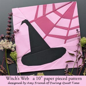 Puede incluir: Un bloque de patchwork de papel rosa y magenta con un sombrero de bruja negro y un diseño de telaraña. El texto "Witch's Web a 10" paper pieced pattern" está en la parte inferior. Diseñado por Amy Friend de During Quiet Time. Mide unos 25 cm.