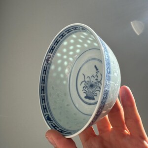 May include: A white porcelain bowl with a blue floral design and a pierced, dotted pattern. The bowl has a blue patterned border and a central floral motif. The bowl is held in a hand.