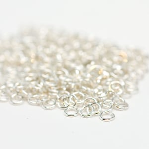 May include: A pile of silver jump rings, a type of jewellery finding used for connecting chains, cords, and other jewellery components.