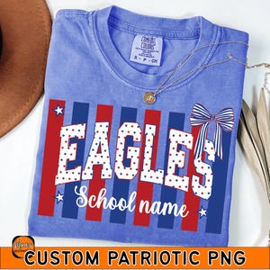 May include: A blue t-shirt with a patriotic design featuring the word "EAGLES" in white letters filled with red and blue stars. Red and blue stripes and a bow accent the design. The words "School name" are below the word "EAGLES".