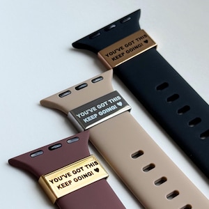 Puede incluir: Primer plano de tres correas de reloj en negro, beige y burdeos. Cada correa tiene una pieza metálica con el texto "YOU'VE GOT THIS KEEP GOING!" y un símbolo de corazón. Las correas son de silicona y tienen múltiples agujeros para ajustar.