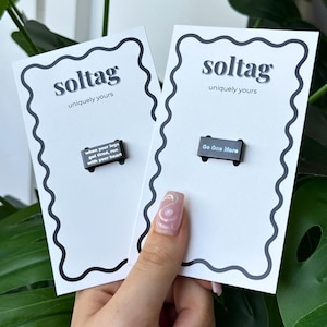 May include: Two black enamel pins on white cards. One pin reads "when your legs get tired, run with your heart." The other pin says "Go One More." The cards have a black wavy border and the text "soltag uniquely yours."