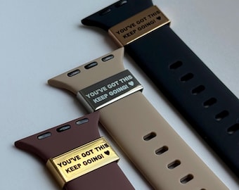 Puede incluir: Tres correas para Apple Watch en negro, beige y marrón. Cada correa tiene una pieza metálica con el texto "YOU'VE GOT THIS KEEP GOING!" en blanco. Las correas están hechas de un material flexible y tienen agujeros de ajuste.