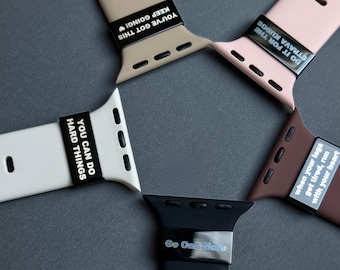 Puede incluir: Una variedad de correas de reloj coloridas en beige, rosa, blanco, marrón y negro. Cada correa presenta una frase motivacional en texto blanco sobre una pieza negra. Frases como "You've Got This" y "Go One More."
