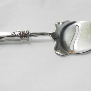 May include: Silver cheese knife with an ornate handle and a serrated blade.