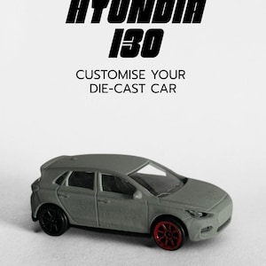 May include: A grey die-cast Hyundai i30 model car with black wheels and red rims. The image includes the text "HYUNDAI i30" and "CUSTOMISE YOUR DIE-CAST CAR". The car is a miniature replica of a hatchback vehicle.