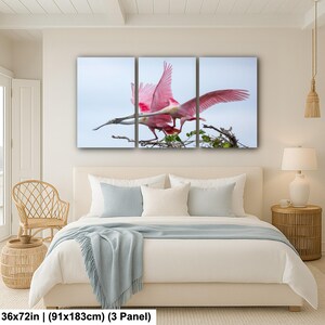 a bedroom with a large bed, a wicker chair, and a painting of a pink bird perched on a branch.