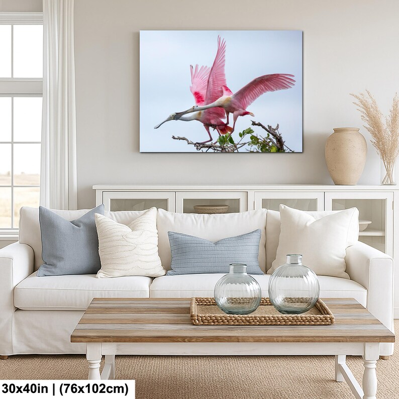 a large, vibrant pink bird with outstretched wings, perched on a branch, with a serene blue sky in the background.