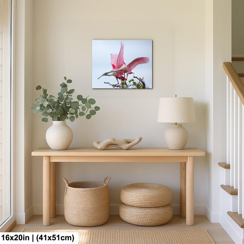 a wooden console table with a lamp, a woven basket, and a framed photograph of a pink bird in flight.