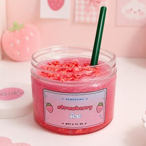 Könnte beinhalten: Ein klares Glas gefüllt mit rosa Schleim und roten Streuseln, mit einem grünen Strohhalm. Das Glas hat ein Etikett mit der Aufschrift "strawberry ice" mit Erdbeer-Illustrationen. Der weiße Deckel trägt das Wort "nomoslime".