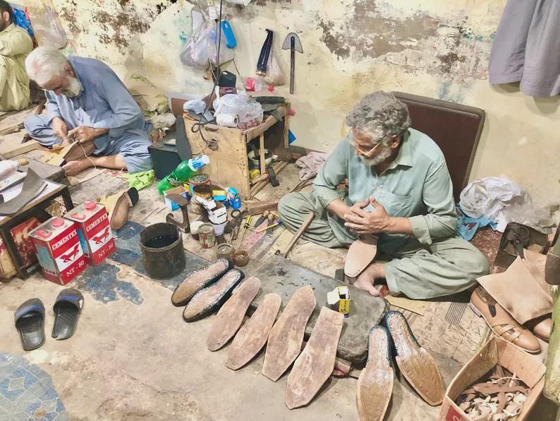 K&ouml;nnte beinhalten: Zwei Schuhmacher arbeiten in einer Werkstatt. Einer sitzt und bearbeitet eine Schuhsohle, w&auml;hrend der andere sitzt und an einem Lederst&uuml;ck arbeitet. Verschiedene Schuhkomponenten und Werkzeuge sind verstreut.