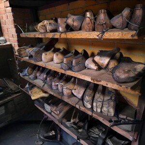 K&ouml;nnte beinhalten: Ein rustikales Holzregal mit verschiedenen antiken Schuhleisten. Die Leisten, in verschiedenen Formen und Gr&ouml;&szlig;en, sind aus dunklem Holz gefertigt und weisen Altersspuren auf. Die Regale stehen vor einer Backsteinmauer.