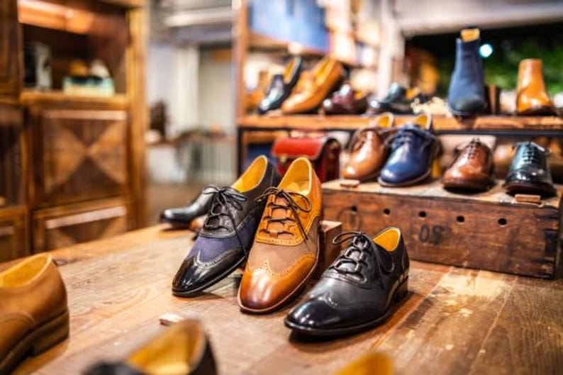 K&ouml;nnte beinhalten: Eine Auswahl an Herrenlederschuhen in verschiedenen Stilen und Farben. Die Abbildung zeigt Oxford-Schuhe, Stiefel und elegante Schuhe in Braun-, Schwarz- und Blaut&ouml;nen. Die Schuhe sind auf einer Holzoberfl&auml;che angeordnet.