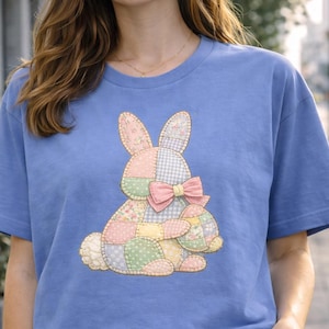 May include: A pale blue t-shirt with a patchwork bunny design, a pink bow, and an Easter egg. The bunny is made of pastel fabrics. The shirt is a casual, short-sleeved style.