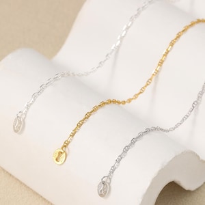 Puede incluir: Tres delicados collares en tonos dorados y plateados se exhiben sobre una superficie blanca y curvada. Cada collar presenta una fina cadena con un pequeño dije decorativo en el extremo. Las cadenas están ligeramente curvadas, mostrando su diseño.