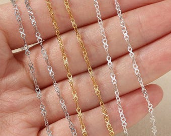 Op de afbeelding: Close-up van verschillende delicate kettingkettingen in zilver- en goudtinten. De kettingen hebben een ingewikkeld oneindigheidsvormig schakelontwerp. De kettingen worden gepresenteerd tegen een neutrale achtergrond, wat hun fijne details en vakmanschap benadrukt.