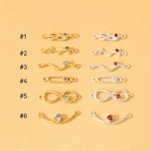 May include: Six pairs of metal jewelry connectors labeled #1 through #6, arranged in two columns. The left column features gold-tone metal pieces, and the right column features silver-tone metal pieces, each set with a small colored gemstone.
