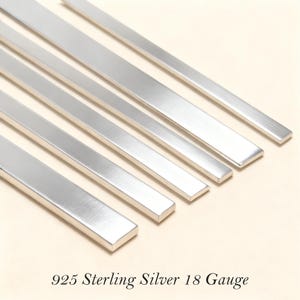Könnte beinhalten: Nahaufnahme von mehreren flachen, rechteckigen Silberstangen. Die Stangen sind diagonal im Bild angeordnet. Der Text "925 Sterling Silver 18 Gauge" befindet sich am unteren Bildrand.
