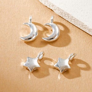 May include: Two silver-toned crescent moon charms and two silver-toned star charms, each featuring a small integrated loop at the top for attachment. These four individual metal jewelry components have a smooth, reflective surface finish.