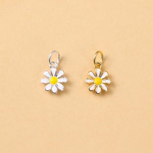 May include: Two daisy flower charms. One is silver-toned with a white and yellow flower. The other is gold-toned with a white and yellow flower. Both have a small loop at the top for attaching to jewellery.