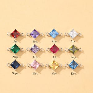 May include: A collection of twelve square-cut gemstone charms in various colors, each with a small loop on either side. Each charm is labeled with a month of the year: Jan., Feb., Mar., Apr., May., Jun., Jul., Aug., Sept., Oct., Nov., and Dec.