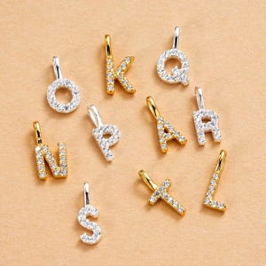 以下が含まれることがあります： キラキラ光るクリスタルがちりばめられた、ゴールドとシルバーのアルファベットチャームのコレクション。チャームには、O、K、Q、N、P、A、R、S、Lの文字と十字架が含まれています。各チャームには、ネックレスやブレスレットに取り付けるための小さなループが付いています。