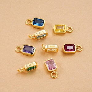 May include: A collection of rectangular gemstone charms in various colors, including blue, yellow, purple, and pink, set in gold-colored metal. Each charm has a small loop for attachment and is marked with "S925".